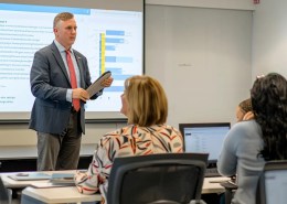 a sleek modern office setting features a confident insurance agent discussing umbrella insurance with a diverse group of clients, highlighted by a large screen displaying crucial statistics and benefits.